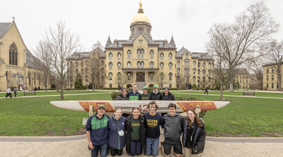 A group of students pose in front of the Golden Dome with their concrete canoe