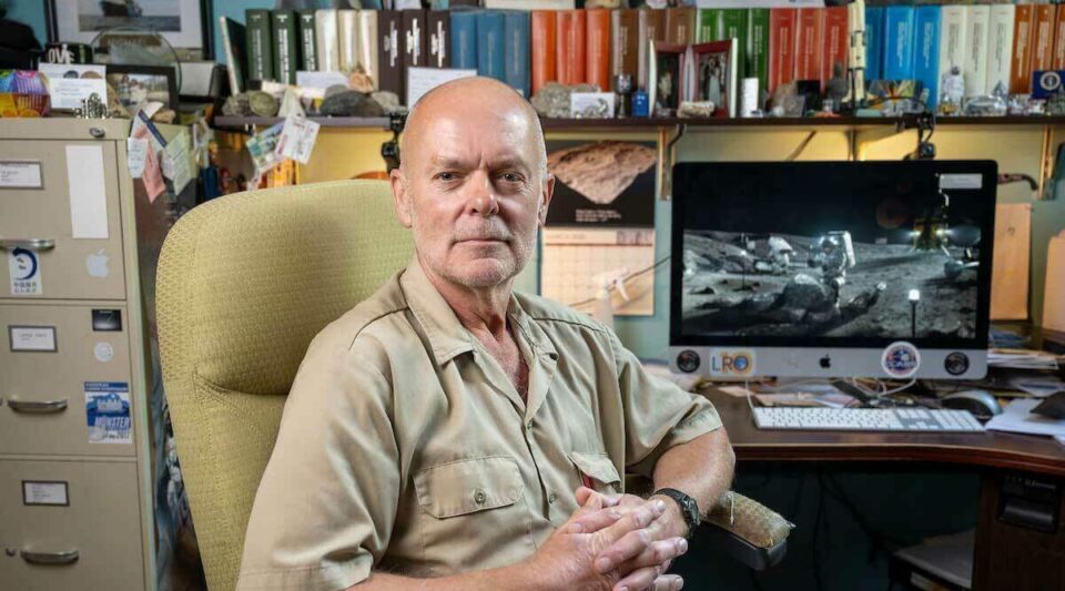 Clive Neal seated in his office at Notre Dame, with a lunar surface image on the computer monitor behind him and shelves of research materials above.