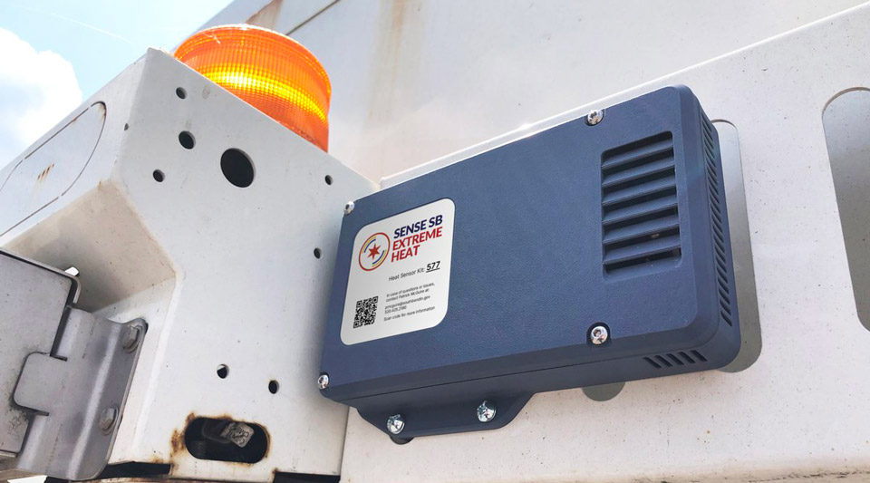 A gray SENSE SB Extreme Heat sensor, labeled "Heat Sensor Kit: 572", mounted on a white garbage truck next to an amber warning light.