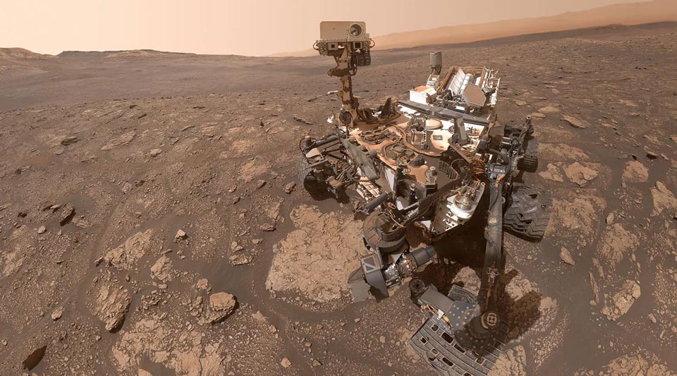 NASA's Perseverance Mars rover sits on a rocky, dusty Martian landscape beneath a hazy orange sky