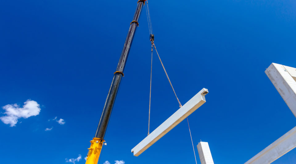 Mobile crane is operating with a huge concrete joist that hangs on chain.