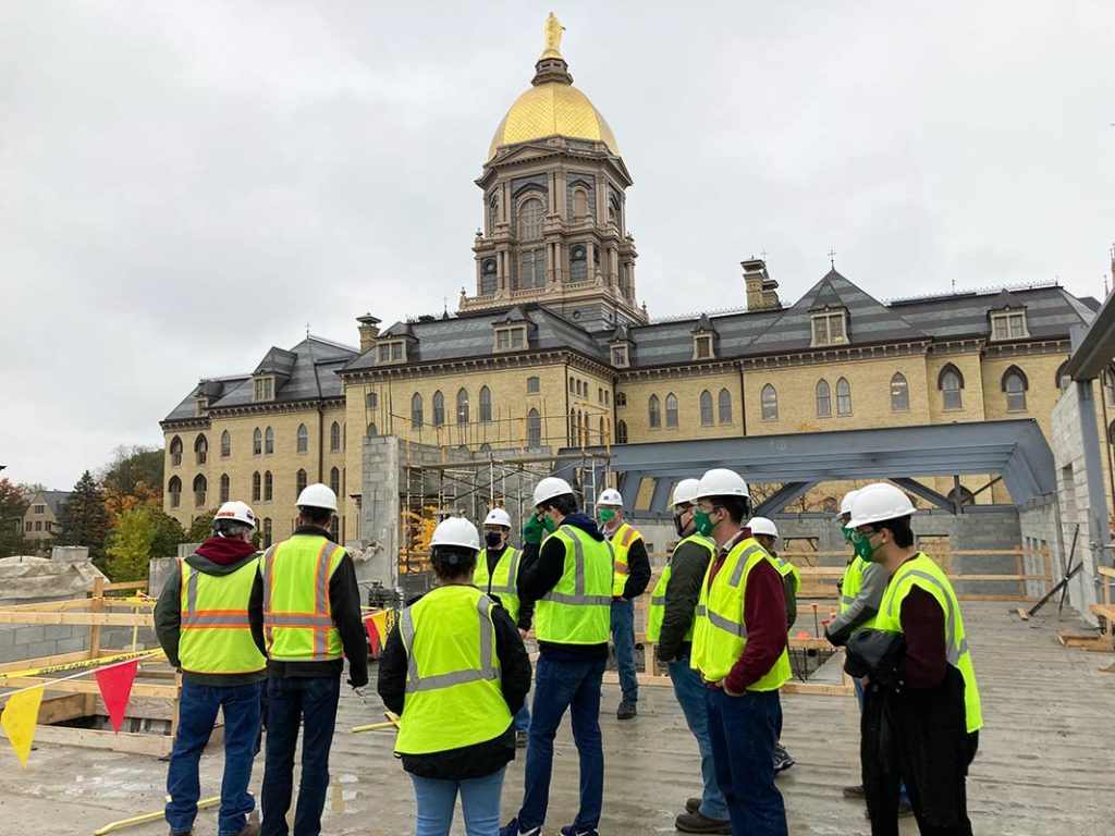 MEng students touring a construction site on campus to investigate the building's load-bearing masonry walls. The Golden Dome is in the background.